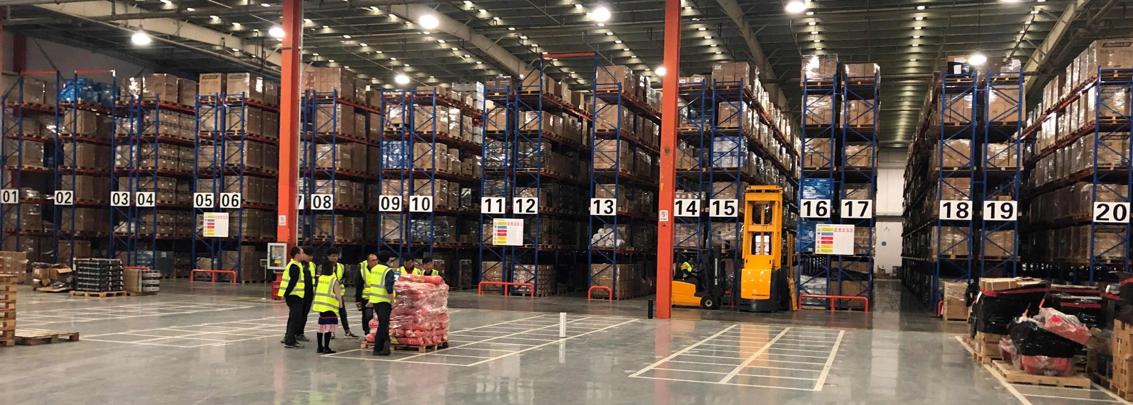 Warehouse with numbered racking bays and workers in high-visibility vests beside a forklift