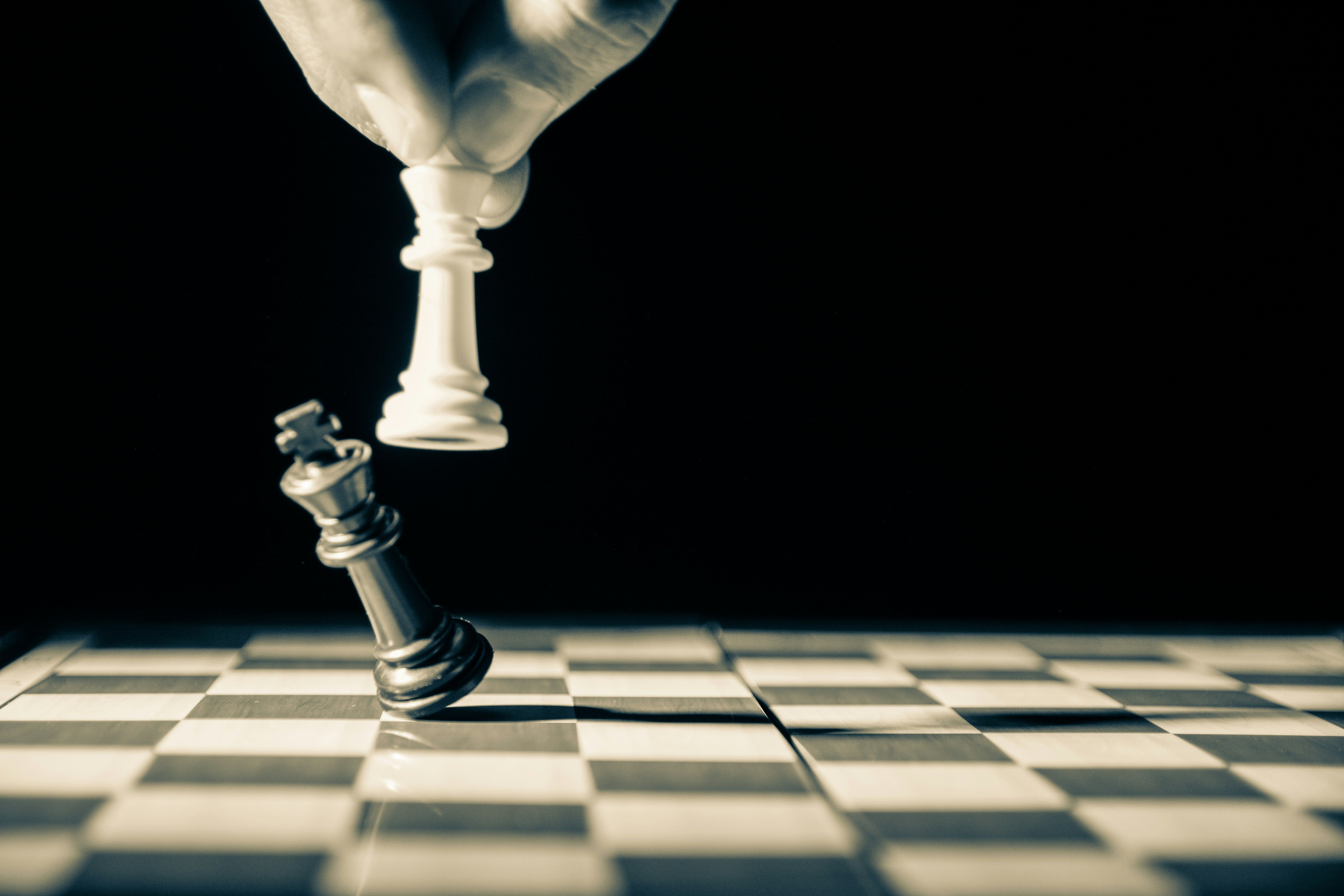 Hand lowering a white chess king toward a toppled black king on a chessboard