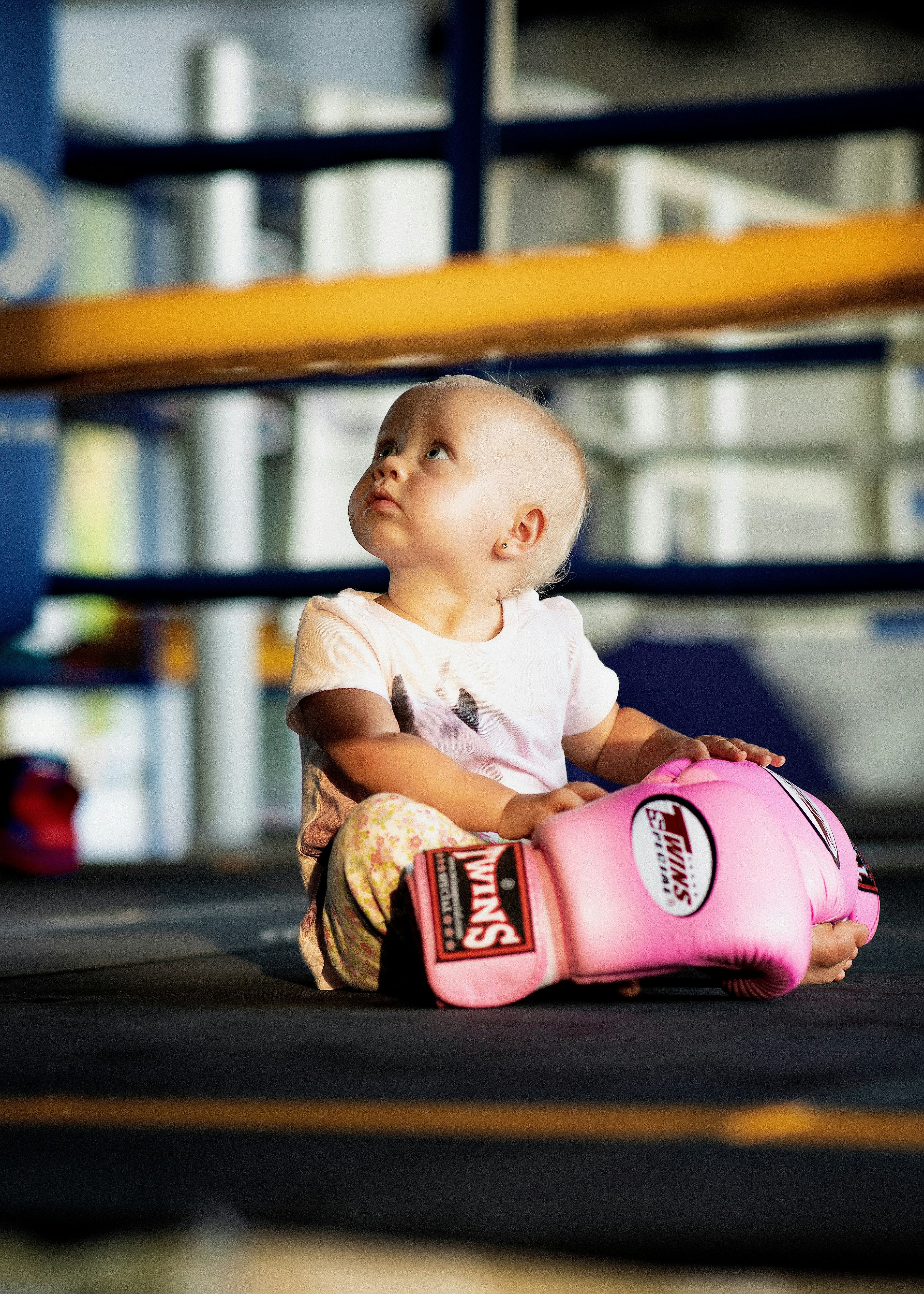 Toddler in a boxing ring sitting beside a pink boxing glove and looking upwards