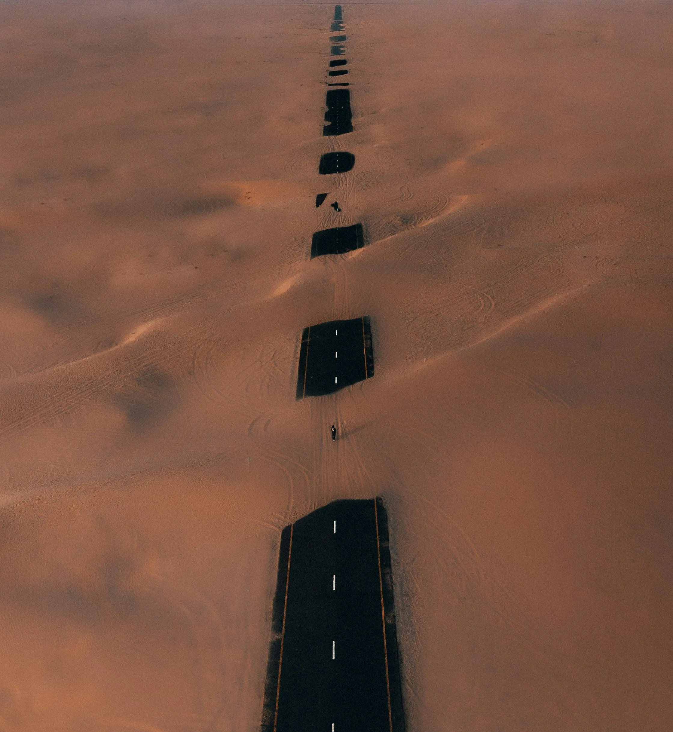 Aerial view of a desert road partly buried under drifting orange sand