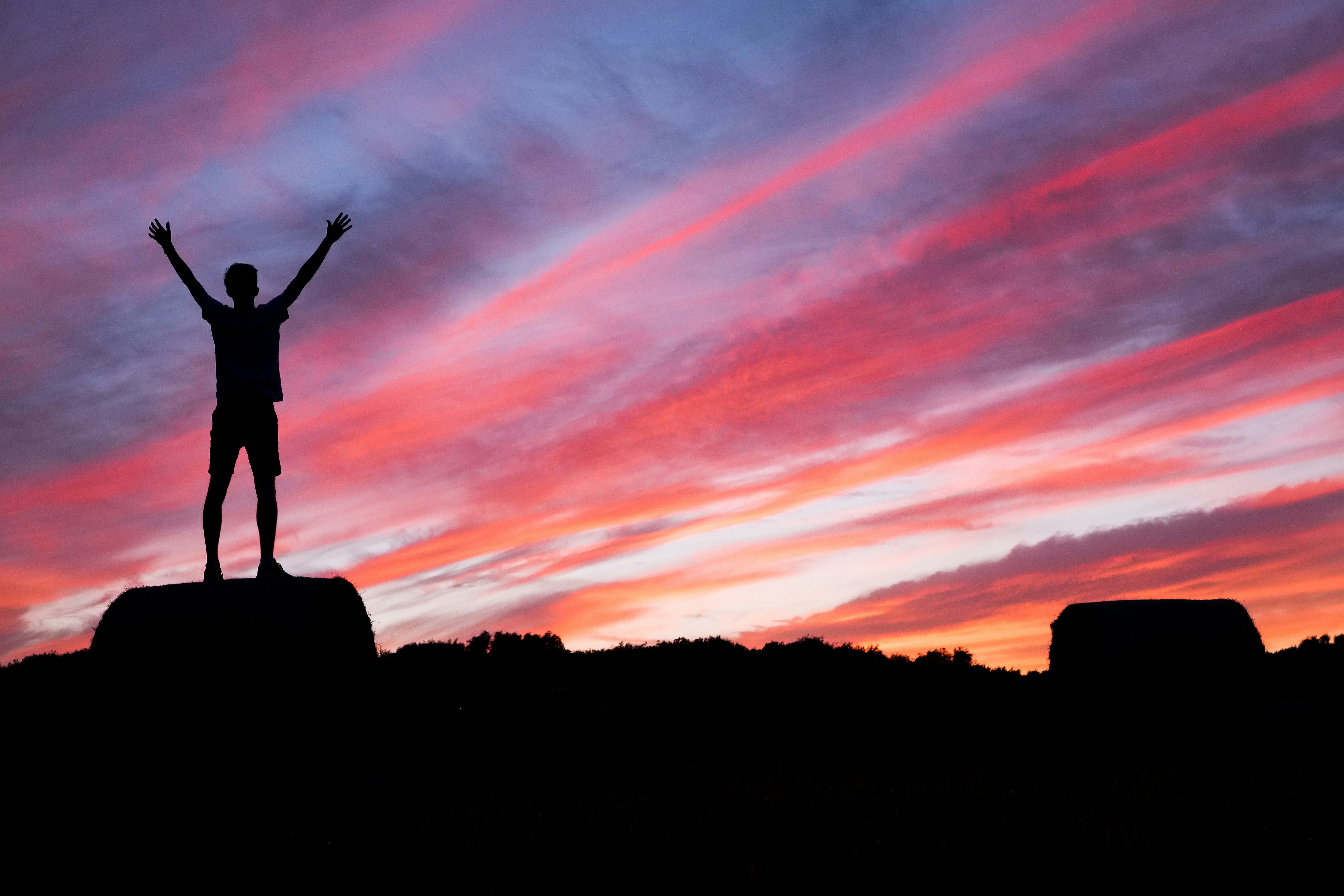 Person standing on a rock with arms raised against a vivid pink and purple sunset sky