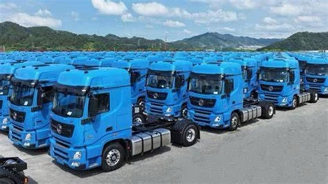 Rows of blue prime mover trucks parked together with green hills behind